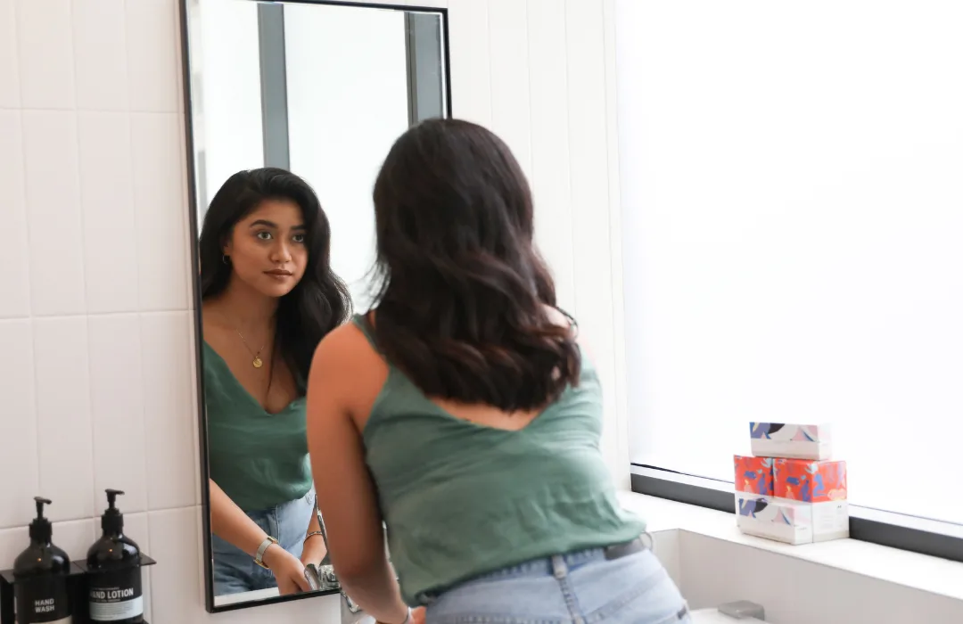 Woman with long hair looking at her reflection in a bathroom mirror