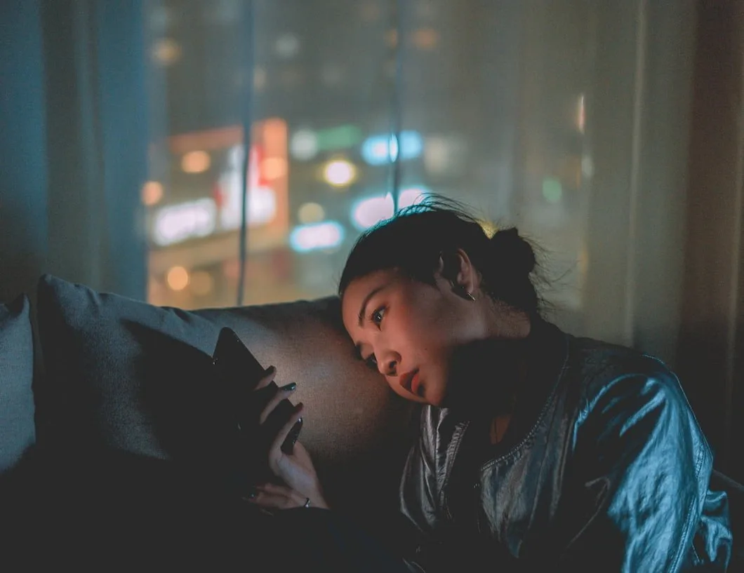 Young woman lying in a dark room lit by her phone screen