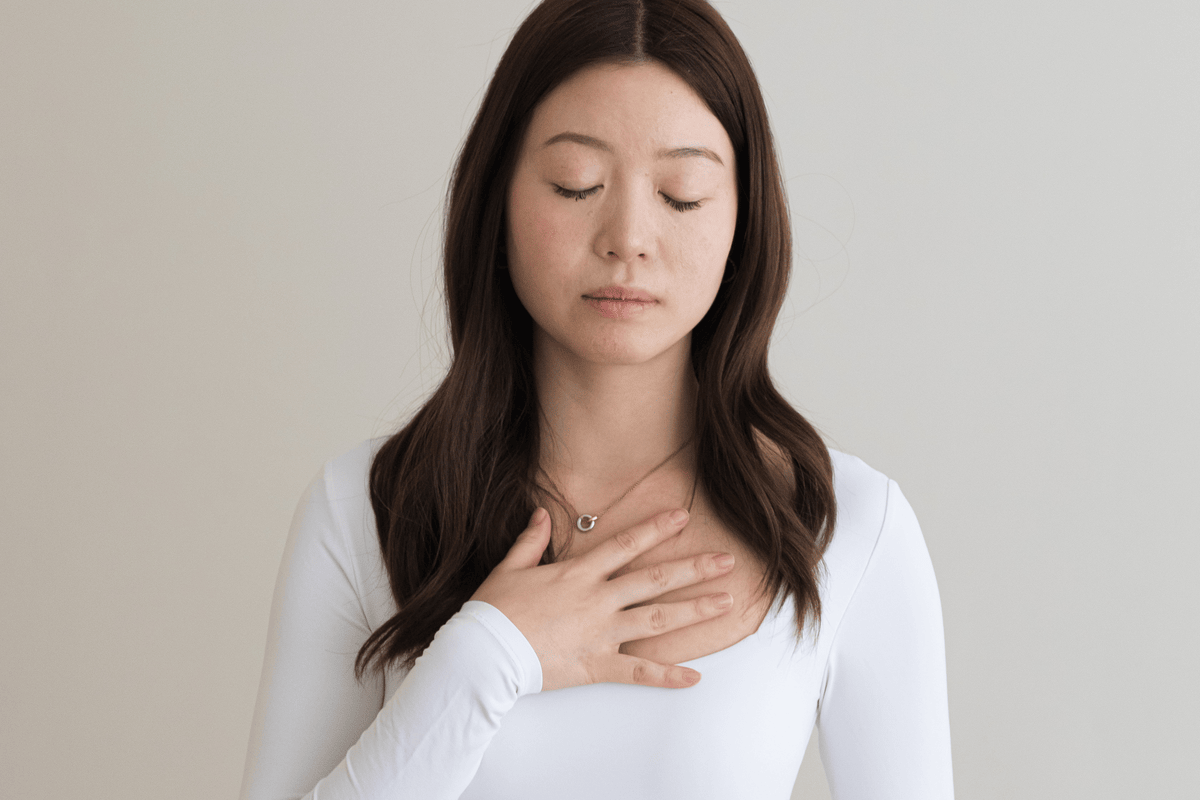 A woman standing with a hand on her heart, eyes closed