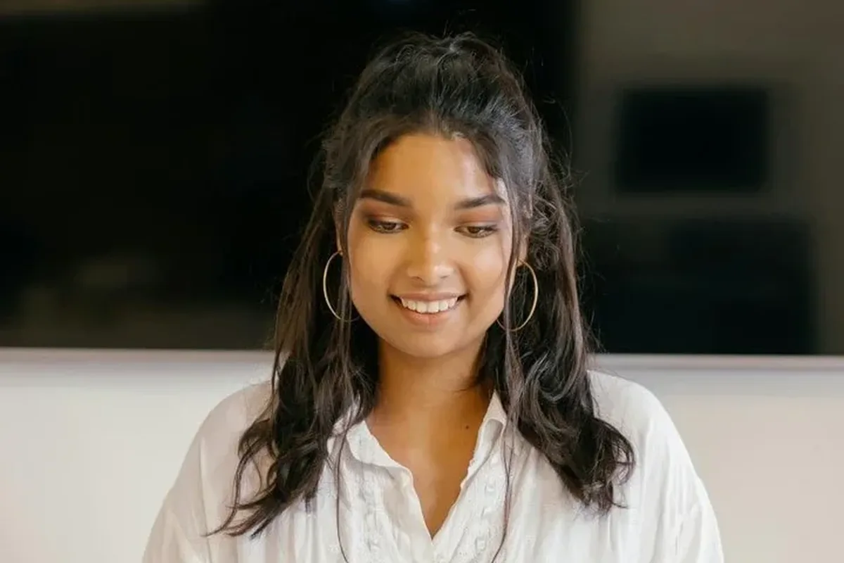 A smiling young woman in a white blouse looking down